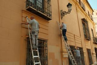 Un artisan réalise le ravalement de façade d'une maison ancienne depuis un échafaudage